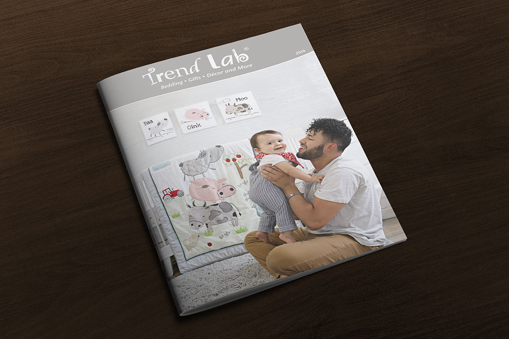 Front cover of Trend Lab 2019 catalog with father holding child in nursery